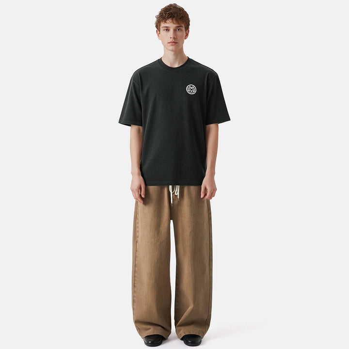 Person wearing a black t-shirt with a logo and brown pants on a white background