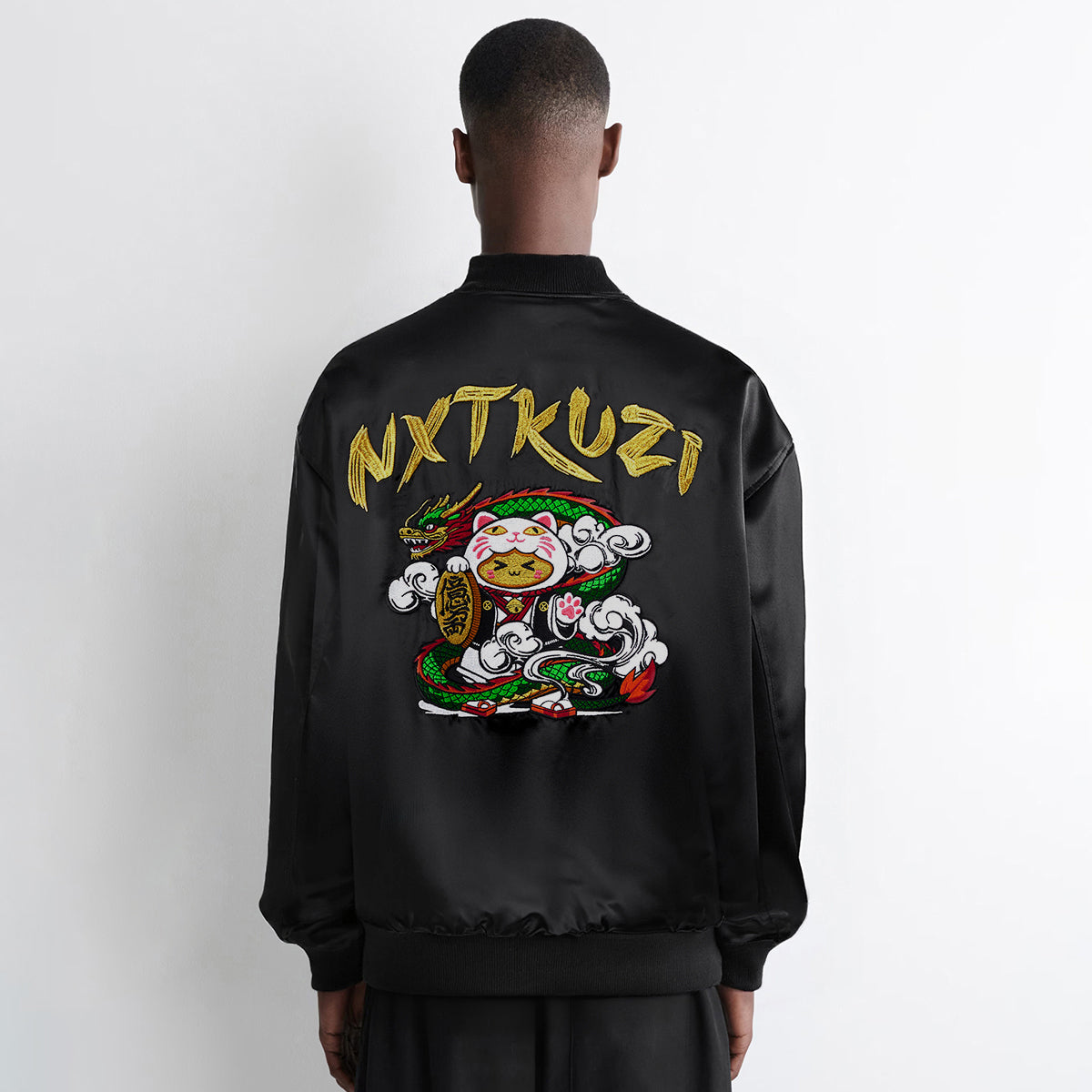 Person wearing a black jacket with 'NXTKUZI' branding on the back against a white background