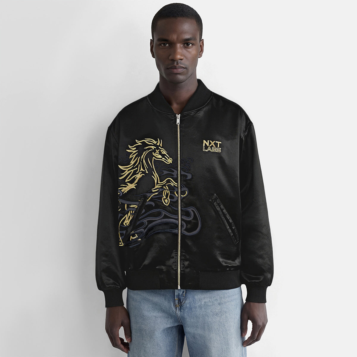 Man wearing a black bomber jacket with gold designs and 'NXT' branding on a white background